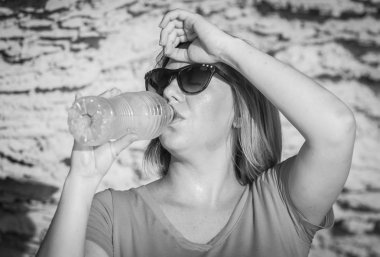 Susuz genç ve çekici beyaz bir kadın güneş gözlüğü tatlı herhangi bir yerinde bir plastik şişe soğuk su içme. Isı kavramı görüntüden acı. Siyah ve beyaz fotoğraf.
