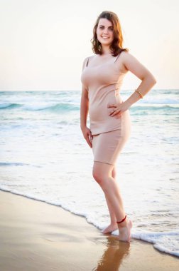 Güzel görünümlü sevimli beyaz elbiseli kız uzun pembe ile fotoğrafçı seyir arka plan üzerinde dalgalar deniz deniz kenarında. Dikey görüntü.