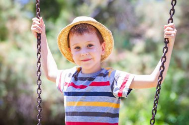 Şirin bir beyaz çocuk çizgili tişört ve salıncakta oynarken bir hasır şapka.