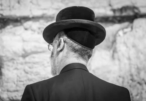 Jewish Orthodox man praying at the Wailing wall, Western wall black and white concept image. A religious Jew in a black hat over a traditional Jewish kippah cap and black suit, traditional Jewish clothing.