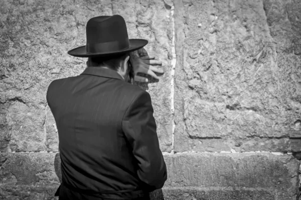 Jewish Orthodox man praying at the Wailing wall, Western wall black and white concept image. A religious Jew in a black hat and black suit, traditional Jewish clothing.
