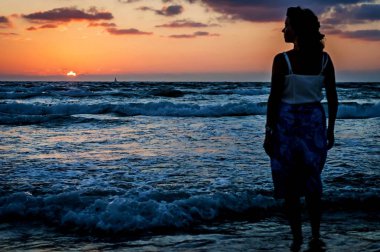 Bir uzun ışık gün batımında gelgit sırasında denize girerek içinde güzel bir genç kadın silüeti. 