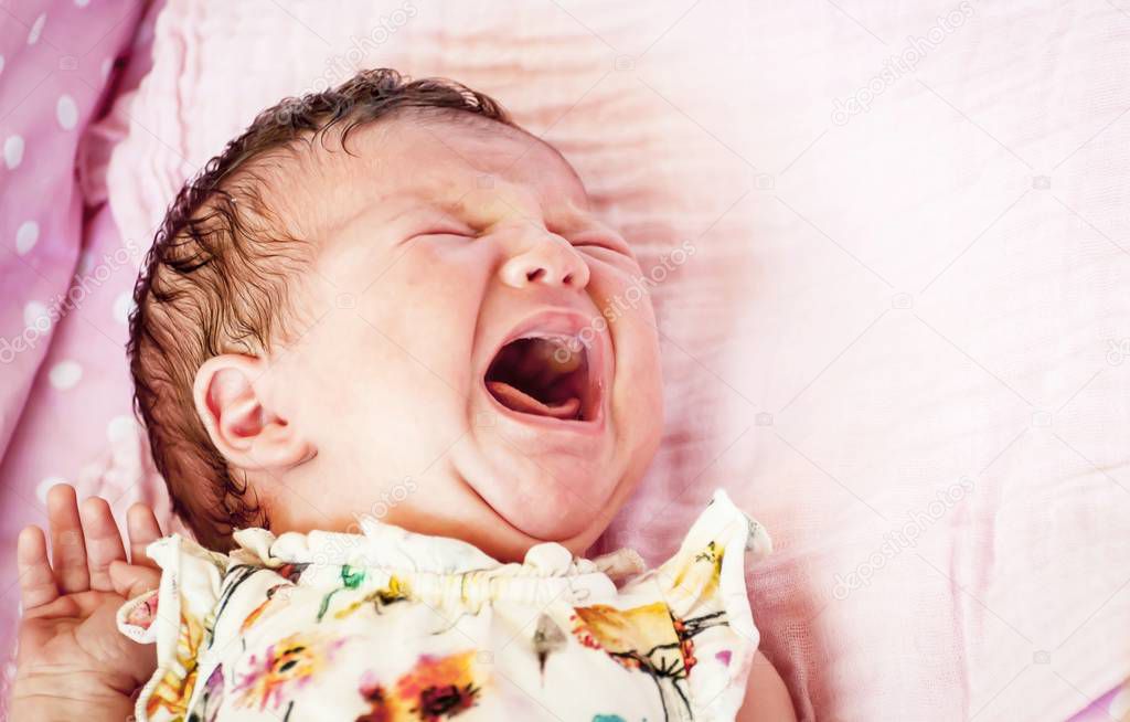 Hungry Caucasian newborn infant baby girl crying hard demanding mother's milk. Crying baby stock image. Open mouth. Stomach cramps, baby colic treatment, infant griping pain, uncomfortable infant intestinal gas symptoms.