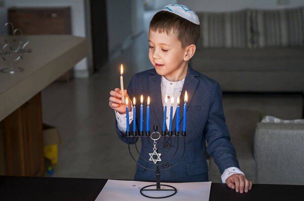 Симпатичный кавказский еврейский мальчик зажигает свечи на традиционной Хануке меноре канделябр, еврейская праздничная концепция
.