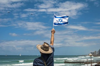 Tel Aviv, İsrail. 9 Mayıs 2019. İsrailli Kafkas adam mavi gökyüzünde askeri uçaklarda bayrak sallayarak ve 71 İsrail Bağımsızlık Günü kavramı havacılık gösterisi izliyor.