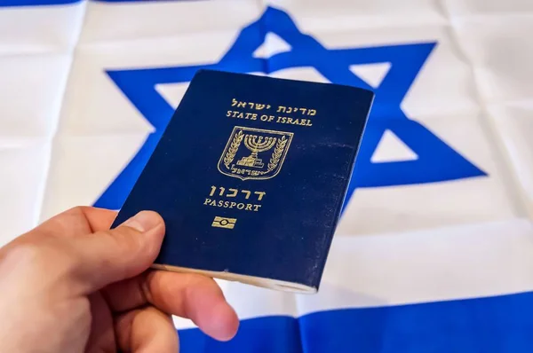 Hand holding the passport of the State of Israel, Israeli flag on the background. Israel citizenship concept, Israeli biometric \