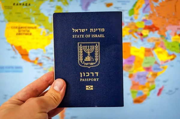 Hand holding the passport of the State of Israel against the colorful world map atlas. Israel citizenship concept, Israeli biometric \