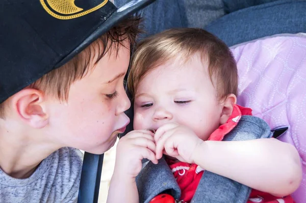 Cute elementary school age Caucasian kid kissing his little baby infant sister. Brother sister love concept.