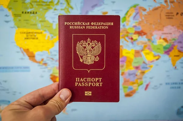 Hand holding the passport of Russia against the colorful world map atlas. Russian passport concept, Russian tourists travel concept.