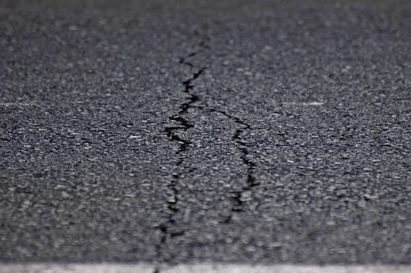 An image of gray asphalt road split by a crack. A metaphor concept for an age crisis, broken dreams, psychological break, marriage relationship problems, shattered trust