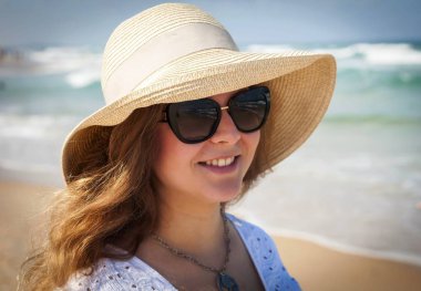 Onu arka planda deniz dalgaları ile deniz kenarında sıcak bir yaz gününde güneş gözlüğü ile bir saman şapka onu geç 20s mutlu güzel genç Kafkas Rus kadın. Deniz konsepti görüntüsünde yaz tatili, mutluluk fikri. Mutlu 30 yaşında yaşlılık
