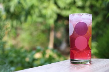 Yeşil bahçe arka planda bir ahşap cam bardakta buz ile soğuk, pembe suyu.