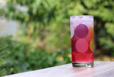 Soğuk, pembe suyu bir damla cam bardakta bir ahşap yeşil bahçe arka planda buz ile.