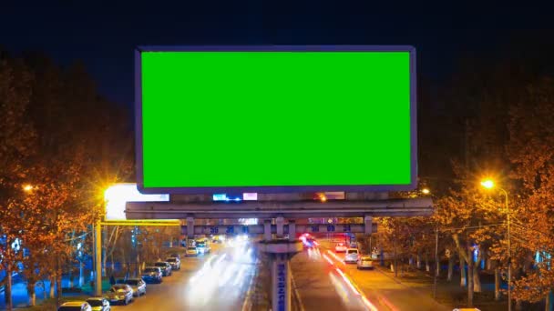 Una cartelera con la llave verde del croma en un fondo de un paisaje nocturno de la ciudad de coches que se mueven rápidamente con la exposición larga. Tiempo de caducidad vídeo — Vídeos de Stock