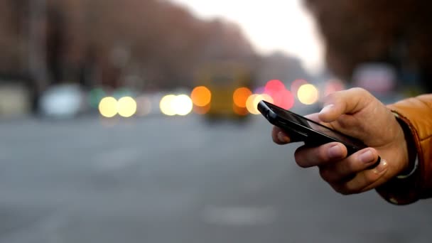 Primo piano della mano maschile utilizzando il telefono cellulare vicino autostrada. Bokeh dei fari dell'automobile — Video Stock