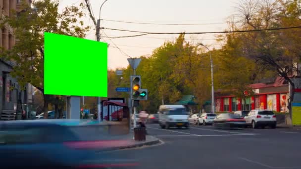 4K Time Lapse video. Big biilboard with green screen the against backgrounds of blurred cars and people in autumn city. The camera moves away — Stock Video