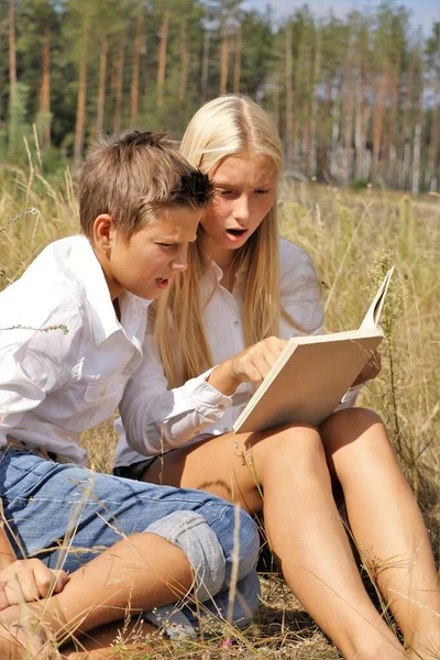 Meisje en jongen in de natuur schoolkinderen lezen een boek in de natuur — Stockfoto