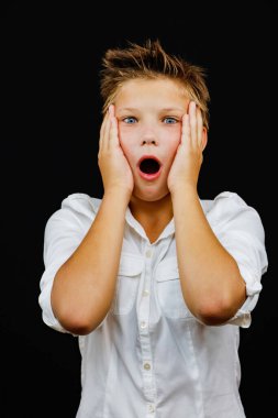 Siyah arka plandaki beyaz gömlekli çocuk korkuyla şaşırdı.