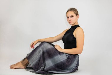 Güzel kız beyaz bir arka planda yerde oturuyor..