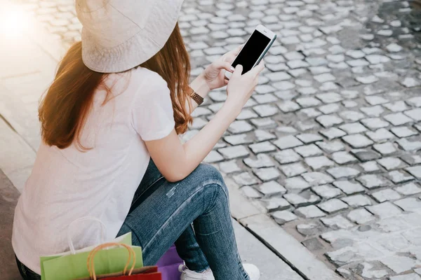 Mutlu cazibe Asyalı kadın alışveriş torbaları ile alışveriş merkezi Smartphone kullanarak