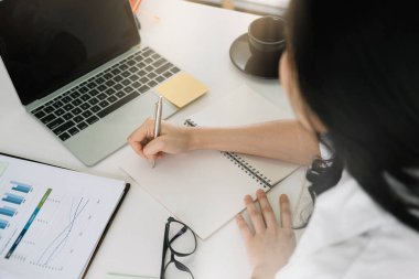 Dizüstü bilgisayarda webinar izlerken not defterine yazan çekici bir kadın.