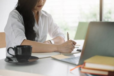 Dizüstü bilgisayarda webinar izlerken not defterine yazan çekici bir kadın.