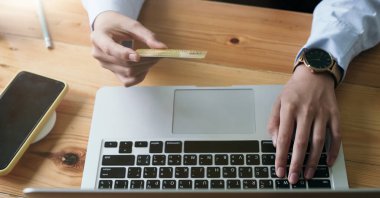 Kredi kartı tutan ve evde dizüstü bilgisayar kullanan bir kadının elini kapat. Çevrimiçi alışveriş kavramı