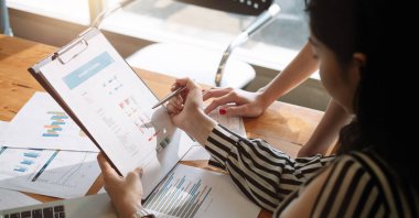 İş adamları ofiste toplanıyor ve bir belge üzerinde tartışıyorlar. İki kadın, iş arkadaşı ile birlikte dizüstü bilgisayarda mali rapor hazırlıyorlar.