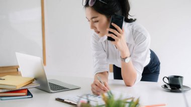 Dizüstü bilgisayarda çalışan ve cep telefonuyla konuşan genç bir girişimci.