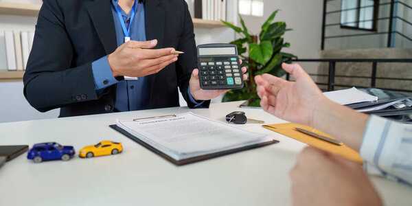 An insurance agent presents a calculator to a client, discussing car insurance calculations and policy details in a professional setting.