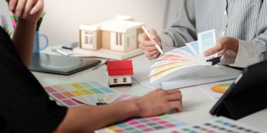 Bir iç mimar ve istemci tasarım danışmanlığı sırasında estetiğe odaklanarak renk örneklerini ve mimari modelleri gözden geçirir.