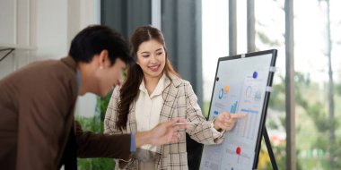 İki meslektaş, parlak bir ofiste iş stratejileri üzerinde işbirliği yaparak, bir sunum tahtasında veri ve eğilimleri analiz ederler..