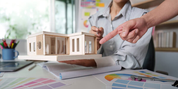 A designer holds a wooden architectural model while discussing design options with a client during a consultation.