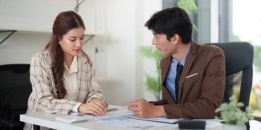 Modern bir ofiste mali raporları ve stratejileri gözden geçiren iki iş adamı arasında odaklanmış bir tartışma.