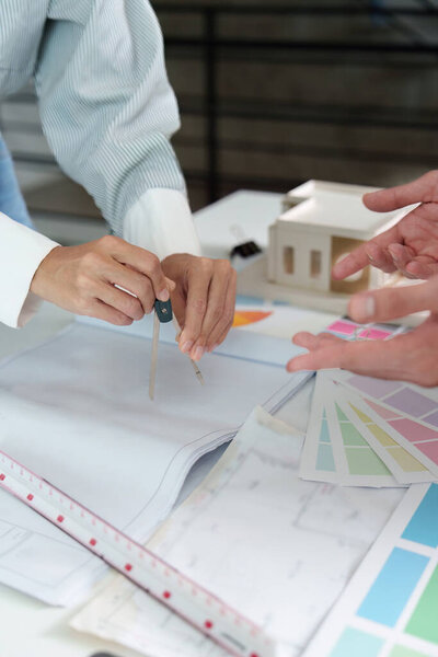 A designer uses a compass to draft plans while discussing color samples during an interior design consultation.
