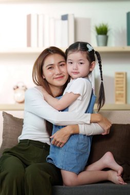 Bir anne ve kızı arasındaki sıcak bir an, rahat bir oturma odasında bağ ve şefkatlerini vurguluyor..