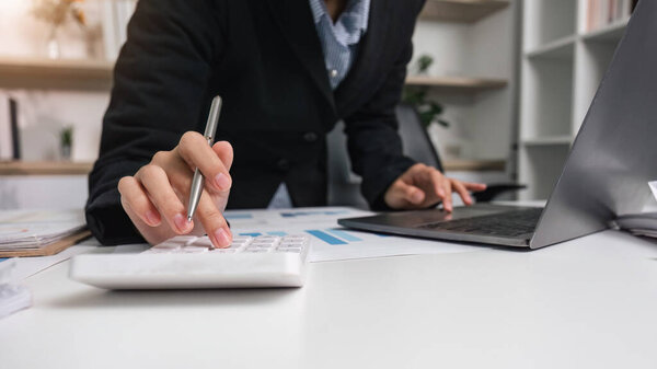 A dedicated accountant using a calculator and laptop to manage financial data and reports in a contemporary office environment.