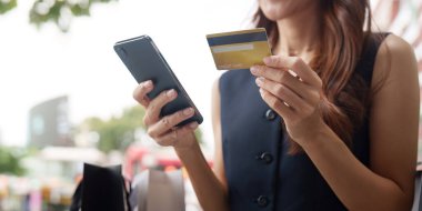 Genç bir kadın ödeme yapmaya hazırlanıyor, elinde bir kredi kartı ve akıllı telefon, modern alışveriş alışkanlıklarını gösteriyor..