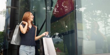 Neşeli bir kadın alışveriş çantalarını tutarken şık bir butiğin önünde alışverişine hayran kalıyor..