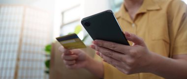 İnternet üzerinden alışveriş yapmak için akıllı telefonu ve kredi kartını kullanan bir kadın modern dijital alışveriş alışkanlıklarını sergiliyor..