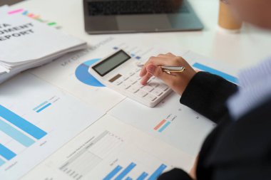 Bir muhasebeci raporlar ve çizelgeler ile çevrili finansal verileri analiz etmek için bir hesap makinesi kullanır. Bütçe ve gider takibine odaklan.