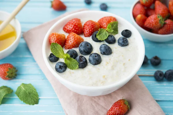 Healthy Breakfast of oatmeal with fresh strawberries, blueberries and honey on a blue background.