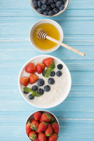 Healthy Breakfast of oatmeal with fresh strawberries, blueberries and honey on a blue background. Top view