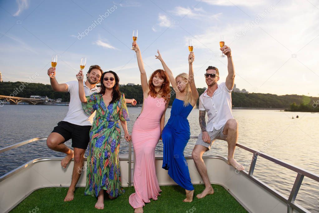 Friends drink champagne and have fun on the yacht during sunset