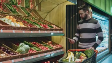 Yaslanmış süpermarket boşaltmak mağaza Dükkanı tüketicilik müşteri yaşam tarzı mutluluk yiyecek satın alışveriş telefonda konuşurken onun alışveriş arabası üzerinde gülümseyen yakışıklı genç