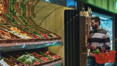 Gıda yerel bakkal mağaza boşaltmak teknoloji aygıt bağlantısı taşıyıcı hareketlilik müşteri satış alışveriş dolu bir sepet ile yürürken onun akıllı telefon kullanan yakışıklı adam