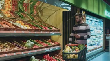 Yakışıklı sakallı adam akıllı telefon onun alışveriş listesine yerel süpermarkette alışveriş yaparken kontrol