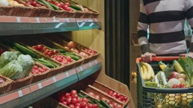 Yakın çekim bakkaliye boşaltmak taze ürün lezzetli vitamini yiyecek vegan vejetaryen yemek sağlıklı yapıyor süpermarkette alışveriş yaparken sebze rafda uzanarak bir adamın kırpılmış 