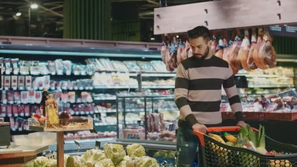 英俊的年轻人购物新鲜的生产在超级市场投入花椰菜入他的购物车 Copyspace 生活方式生命力素食主义素食者健康节食吃消费主义顾客 — 图库视频影像