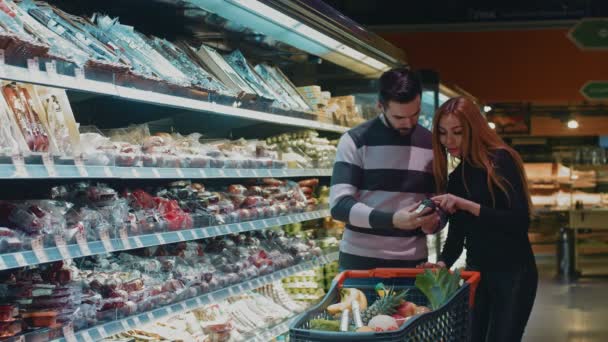 美丽的少妇买食物与她英俊的丈夫一起购物在超级市场 Copyspace 爱家庭团结结合消费主义者销售情侣婚姻客户 — 图库视频影像